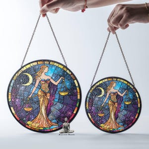 May include: Two round stained glass window hangings featuring a woman holding scales. The larger hanging is 12 inches in diameter and the smaller hanging is 8 inches in diameter. Both hangings feature a colorful mosaic design with a dark blue background and a crescent moon.