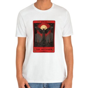 May include: White t-shirt featuring a red tarot card design with a black mothman figure and the text "XVIII THE MOTHMAN" on the card.