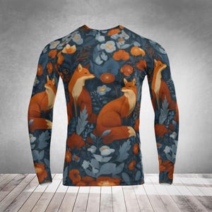 Op de afbeelding: Shirt met lange mouwen met een herhalend patroon van vossen en bloemmotieven. De achtergrond van het shirt is donkerblauw, met oranje en witte bloemen en bladeren. De vossen zijn afgebeeld in tinten oranje en crème.