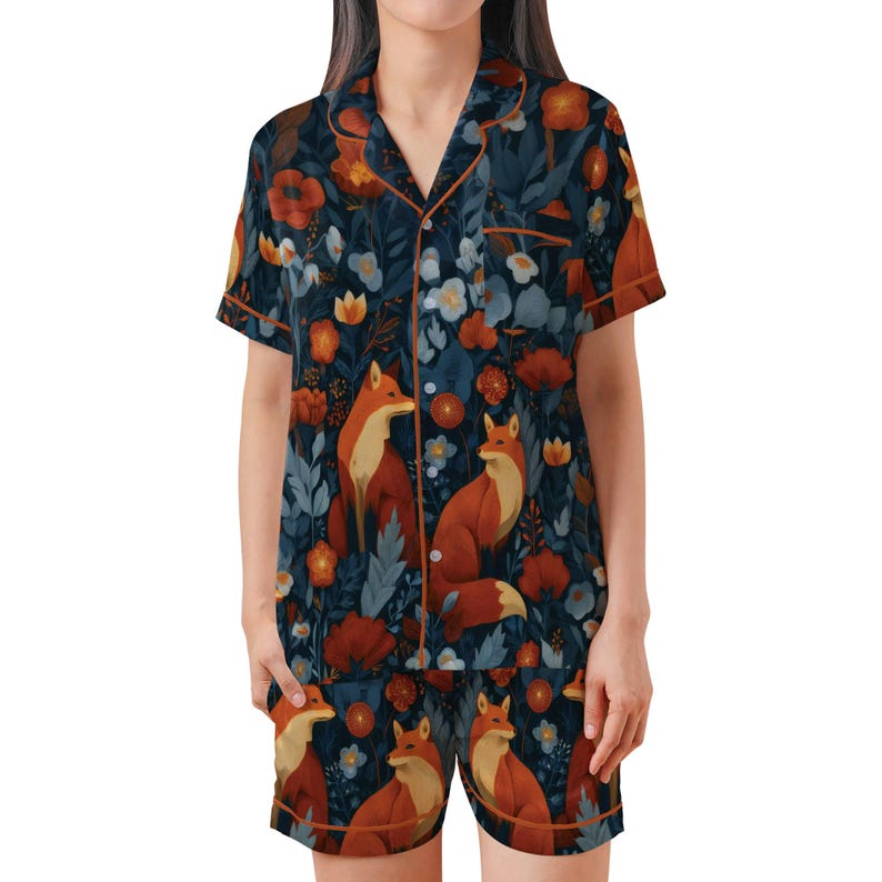 Puede incluir: Un conjunto de pijama de dos piezas con un estampado floral y de zorro azul oscuro. La parte superior de manga corta y los pantalones cortos tienen ribetes naranjas. El dise&ntilde;o incluye zorros naranjas, flores rojas y naranjas y elementos florales blancos y azules.
