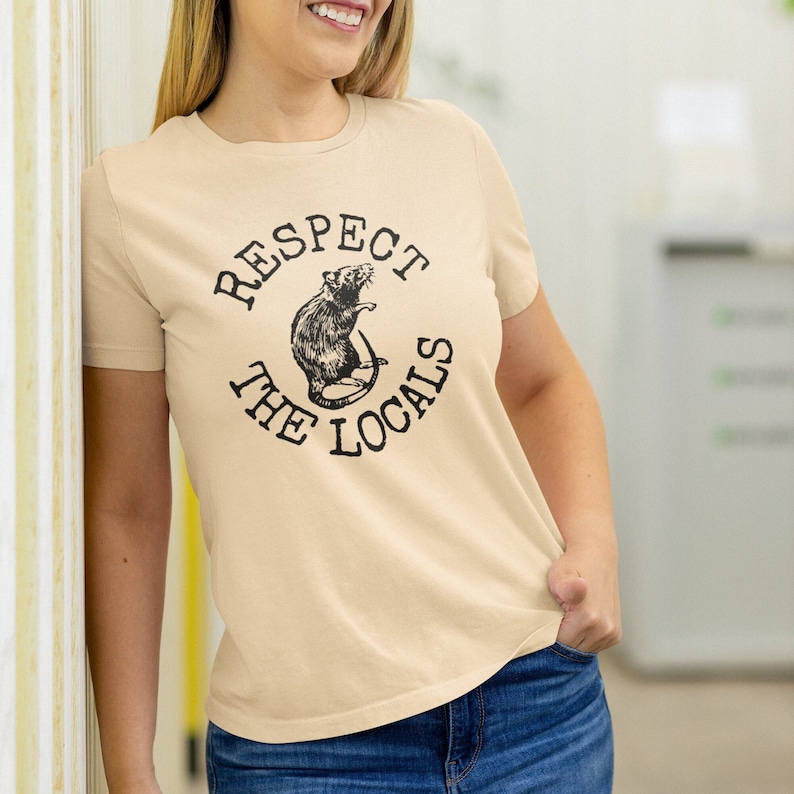 May include: A beige t-shirt with a black graphic of a rat and the text "Respect the Locals".