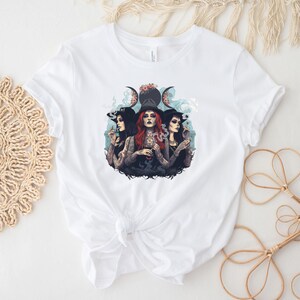 Puede incluir: Camiseta blanca con un gr&aacute;fico de tres mujeres con sombreros de bruja y fumando. Las mujeres est&aacute;n rodeadas de humo y un s&iacute;mbolo de triple luna con flores.