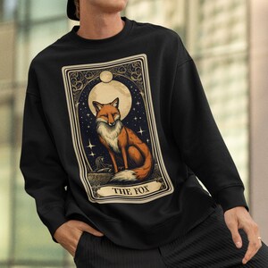 May include: Black sweatshirt featuring a vintage-style illustration of a fox in front of a full moon and stars. The illustration is framed with an ornate border and the text "THE FOX" is printed below the image.