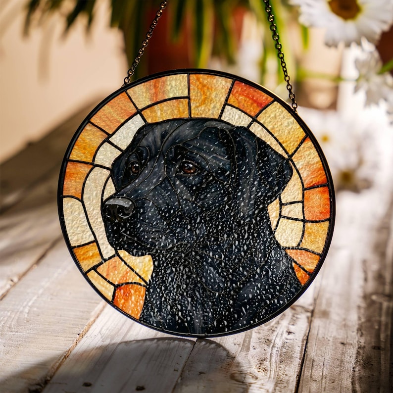 May include: Round stained glass window featuring a black Labrador Retriever. The dog's portrait is set against a background of orange and yellow glass, framed by a black metal border. A decorative chain is attached for hanging.