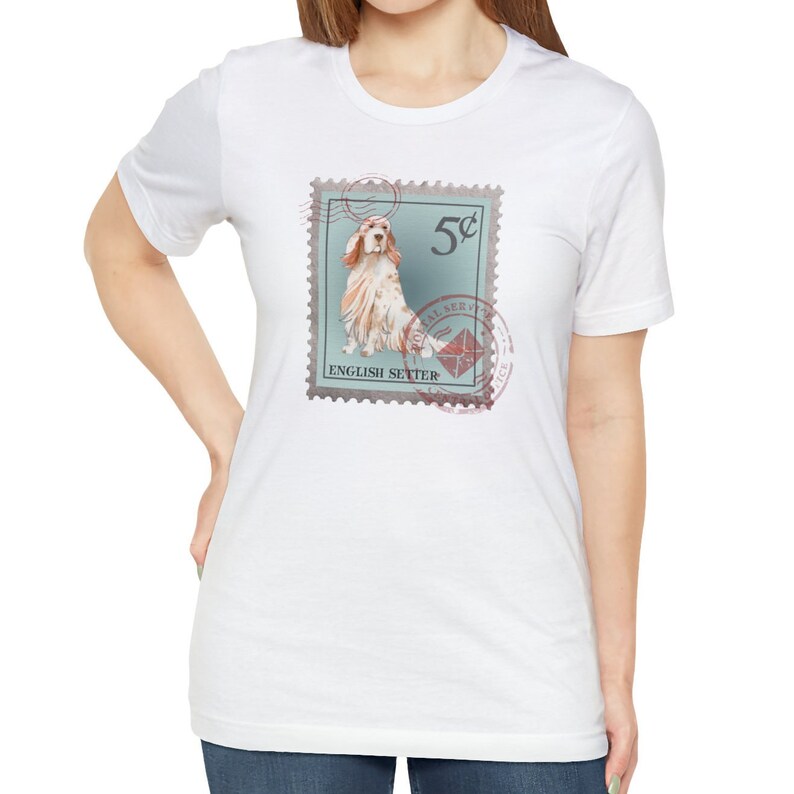 Op de afbeelding: Wit T-shirt met een postzegelontwerp met een illustratie van een Engelse Setter. De postzegel is lichtblauw met de tekst "5&cent;" en "ENGLISH SETTER". Het shirt heeft korte mouwen en een ronde hals.