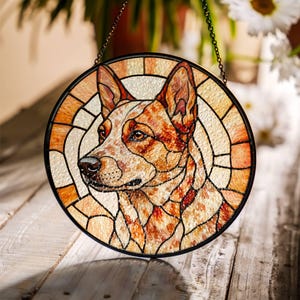 May include: Round stained glass window featuring a dog's portrait. The dog has red and white fur, with a black outline. The glass is segmented with a black border and a chain for hanging. The background is a light beige.