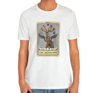 May include: White t-shirt with a graphic of a tarot card featuring a Jackalope, a mythical rabbit with antlers, against a gray background. The card is labeled "XXVIII THE JACKALOPE".