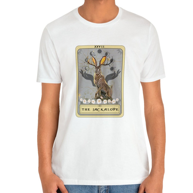 May include: White t-shirt with a graphic of a tarot card featuring a Jackalope, a mythical rabbit with antlers, against a gray background. The card is labeled "XXVIII THE JACKALOPE".