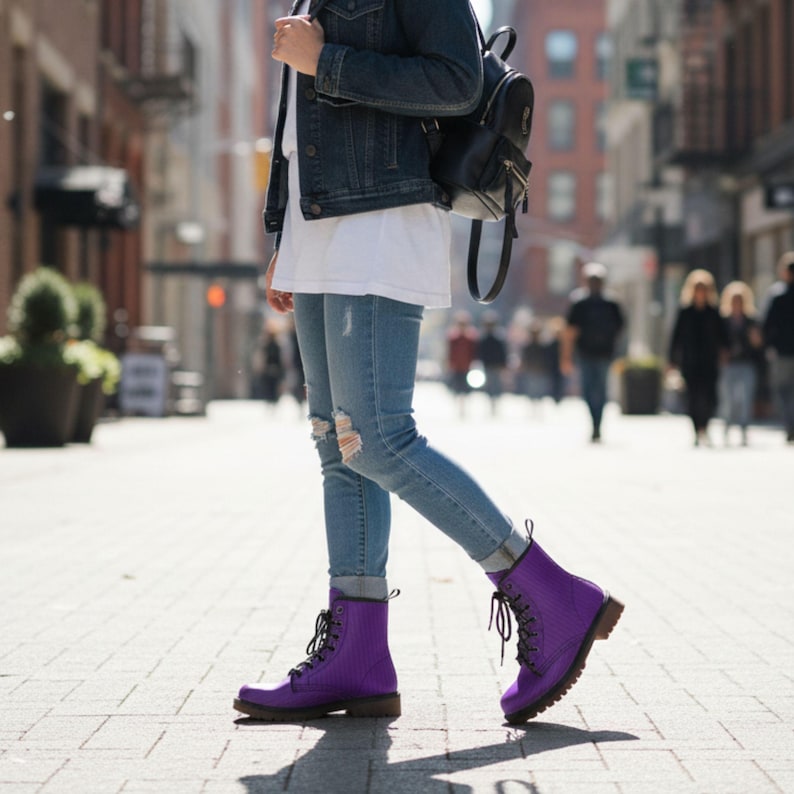 May include: A person walking down a city street wearing light blue ripped jeans and purple lace-up boots. The boots have a textured finish and dark brown soles. A black backpack and denim jacket complete the outfit.