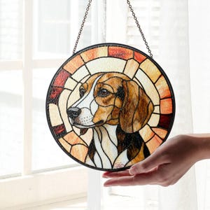 Könnte beinhalten: Rundes Buntglasfenster mit einem Beagle-Hundeporträt. Das Kunstwerk verwendet Braun-, Weiß- und Schwarztöne mit einem segmentierten Design. Ein schwarzer Metallrahmen und eine Kette dienen zum Aufhängen.
