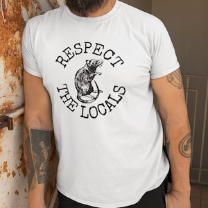 May include: White t-shirt with a black graphic of a rat and the text "Respect the Locals".