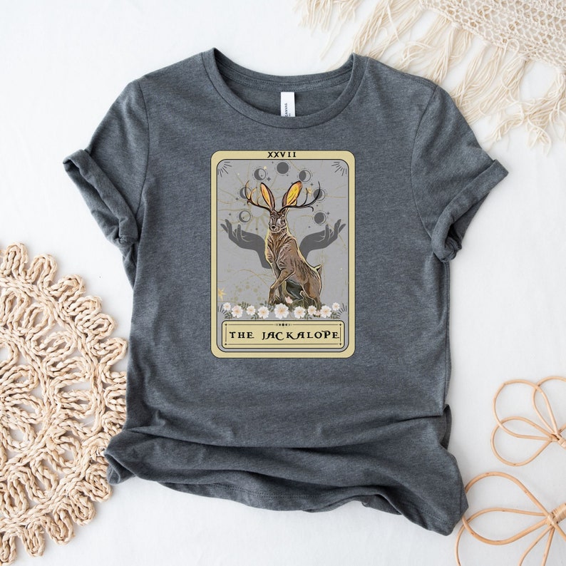 May include: Gray t-shirt with a graphic of a tarot card featuring a Jackalope with antlers and the text "XXVII THE JACKALOPE".