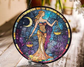 May include: A stained glass window hanging with a chain. The window is round and features a colorful depiction of the astrological sign Libra, a woman holding scales, against a starry night sky background.