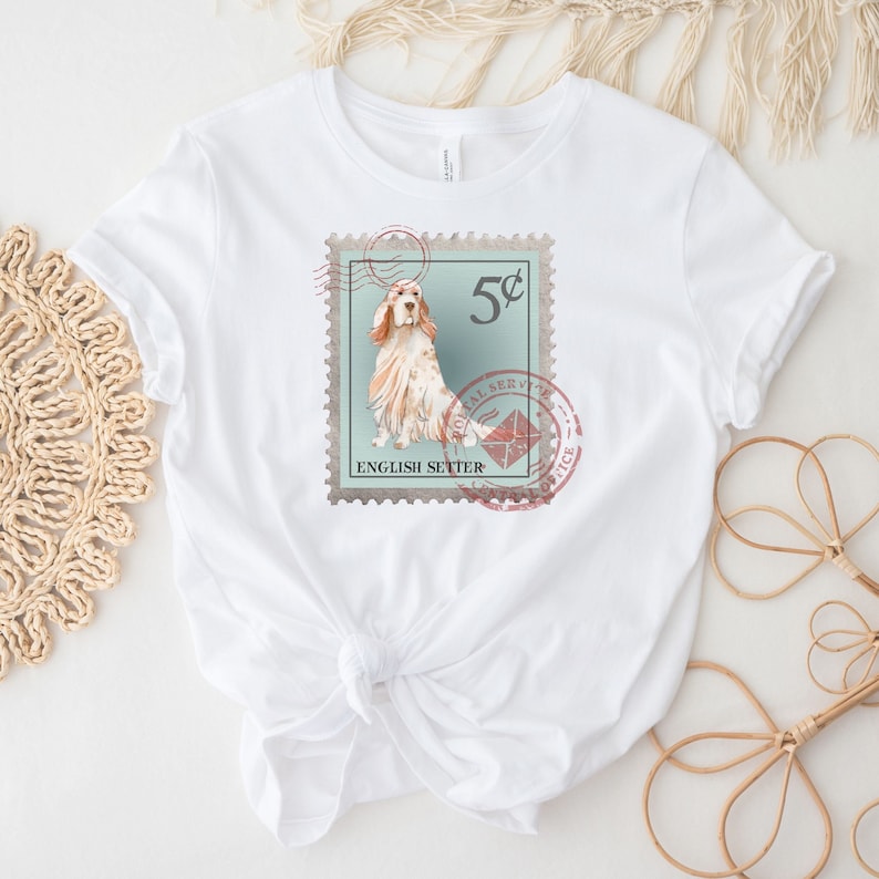 Op de afbeelding: Wit T-shirt met een vintage postzegelontwerp. De postzegel toont een illustratie van een Engelse Setter hond, een waarde van 5 cent en de woorden "Postal Service Office" en "English Setter".