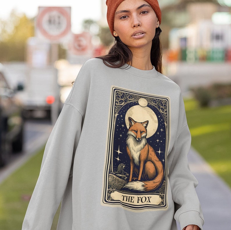 May include: A grey sweatshirt featuring a graphic print of a fox in a moonlit forest. The graphic is in a vintage style and includes the text "THE FOX".