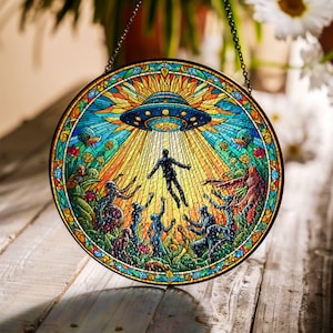 Può includere: Una finestra in vetro colorato appesa con una cornice circolare che raffigura un disco volante con un raggio di luce che illumina una persona con le braccia aperte. La persona è circondata da altre figure che tendono le braccia verso la luce.