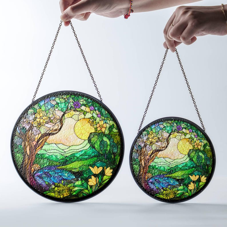Op de afbeelding: Twee ronde gebrandschilderde zonvangers met een natuurtafereel. De grotere zonvanger heeft een boom met groene bladeren en een gele zon. De kleinere zonvanger is hetzelfde ontwerp, maar kleiner.