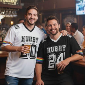 Puede incluir: Dos camisetas de estilo f&uacute;tbol, una blanca y otra negra, con "HUBBY" impreso en el pecho. La camiseta blanca tiene el n&uacute;mero "20" y la negra el "24". Ambas tienen rayas de arco&iacute;ris en las mangas.