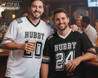 Puede incluir: Dos camisetas de estilo fútbol, una blanca y otra negra, con "HUBBY" impreso en el pecho. La camiseta blanca tiene el número "20" y la negra el "24". Ambas tienen rayas de arcoíris en las mangas.