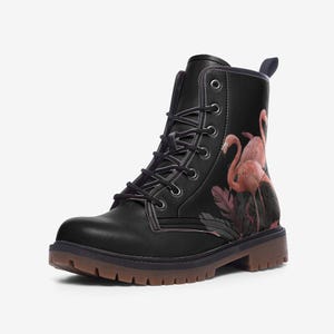 May include: Black combat boot featuring a pink flamingo design. The boot has a lace-up closure, a brown sole, and a pull tab at the back. The flamingo design includes pink birds and foliage.