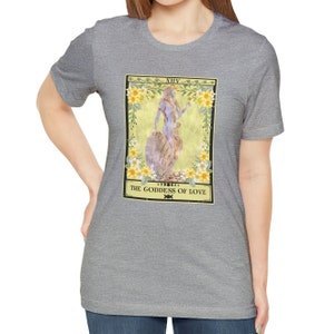 May include: A heather grey t-shirt with a tarot card design featuring a woman standing on a shell with flowers and the text "XIV THE GODDESS OF LOVE".