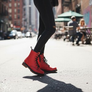 May include: Red leather boots with black laces and a textured design. The boots are worn with black jeans. The image is taken outdoors on a sunny day, with a city street in the background.