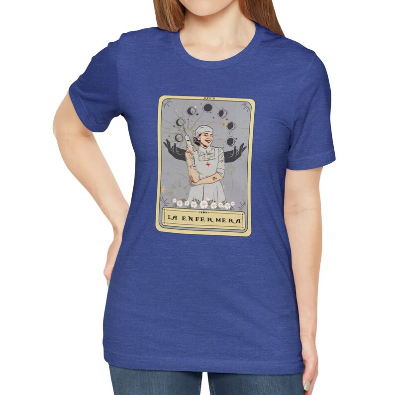 May include: A blue t-shirt featuring a tarot card design with a woman in a nurse's uniform holding a syringe. The card is titled "La Enfermera" in Spanish.