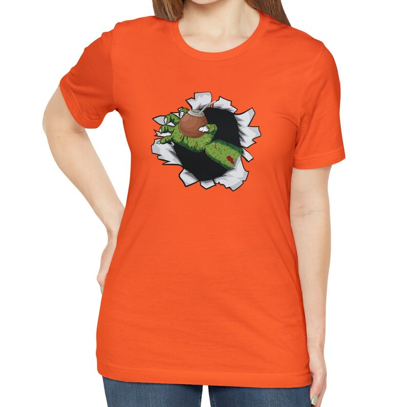 May include: Orange t-shirt with a graphic of a green zombie hand reaching out of a ripped hole in the fabric, holding a brown cup with a straw.