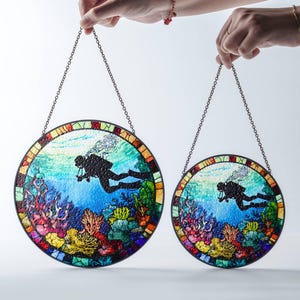Op de afbeelding: Twee ronde gebrandschilderde raamhangers met een moza&iuml;ekontwerp. De grotere hanger toont een duiker in een blauwe oceaan met koraalriffen. De kleinere hanger is hetzelfde ontwerp, maar kleiner.