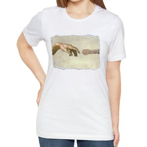 May include: A white t-shirt with a graphic of a tiger paw and a human hand reaching out to touch it, referencing the famous "Creation of Adam" painting.