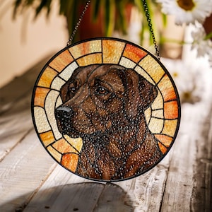 May include: Round stained glass window featuring a brown Labrador Retriever dog. The dog's portrait is framed by a segmented design in shades of orange, yellow, and cream. A black chain is attached for hanging.