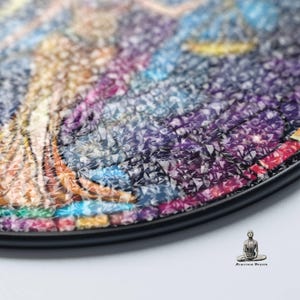 May include: Close-up of a round, colorful mosaic art piece with a black frame. The mosaic is made of small, iridescent tiles that create a textured surface.