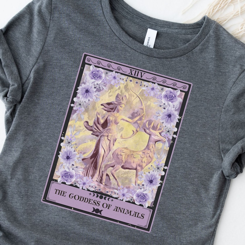 May include: A purple and white tarot card with a woman holding a bow and arrow, standing next to a deer. The card is titled "The Goddess of Animals" and has the number XIV on it.