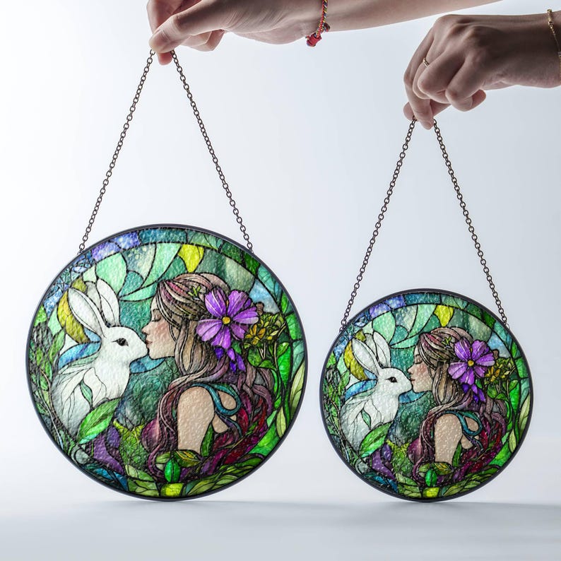 Op de afbeelding: Twee gebrandschilderde zonvangers met een fantasierijk ontwerp van een vrouw en een konijn. De grotere zonvanger toont een vrouw met lang, golvend haar en een konijn met witte vacht. De kleinere zonvanger heeft een vergelijkbaar ontwerp, maar is kleiner.
