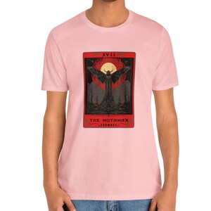 May include: A pink t-shirt featuring a tarot card graphic of a winged creature with the text "XVIII THE MOTHMAN".