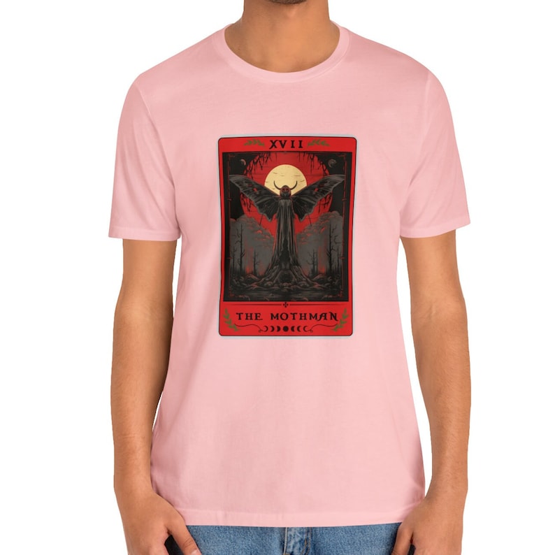 May include: A pink t-shirt featuring a tarot card graphic of a winged creature with the text "XVIII THE MOTHMAN".