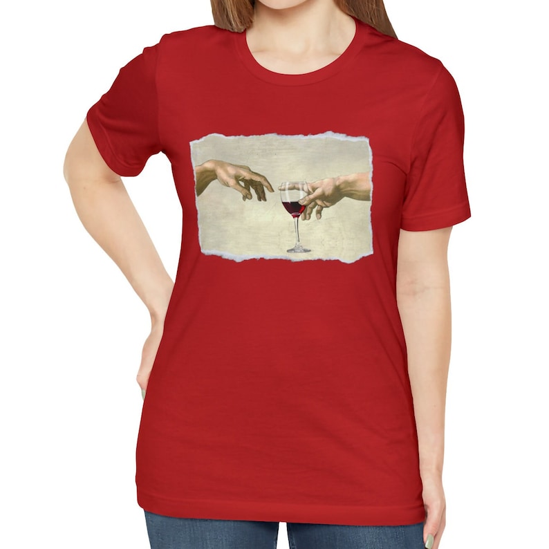 May include: Red t-shirt with a white graphic of two hands reaching towards each other, holding a glass of red wine. The graphic is a parody of the famous "The Creation of Adam" painting.