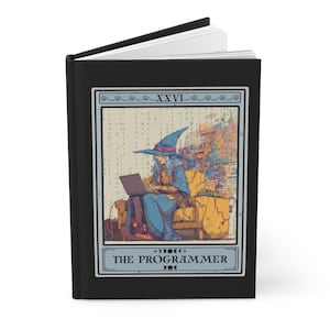 May include: Black journal with a tarot card illustration. The card shows a figure in a wizard hat using a laptop, labelled "The Programmer." The artwork has a digital art style with a colour palette of blues, yellows, and browns.
