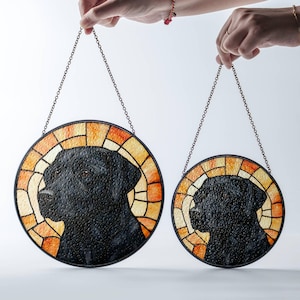 May include: Two round stained glass dog portraits. The black dog silhouettes are set against a mosaic of orange, yellow, and cream-colored glass. Each piece is framed in black and hangs from a chain.