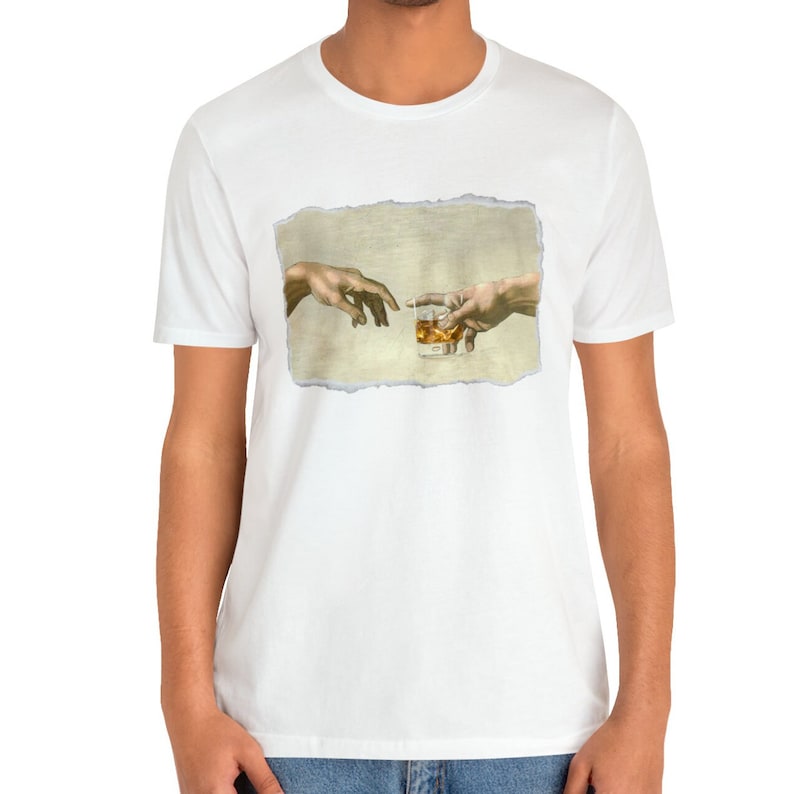 K&ouml;nnte beinhalten: Ein wei&szlig;es T-Shirt mit einem Aufdruck von zwei H&auml;nden, die sich gegenseitig erreichen und ein Glas Whisky halten. Der Druck ist im Vintage-Stil mit einem abgenutzten Look.