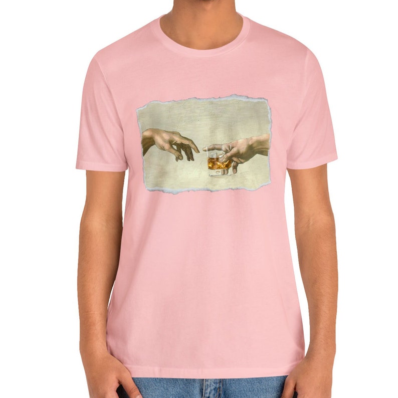 K&ouml;nnte beinhalten: Ein pinkfarbenes T-Shirt mit einem Grafikdruck von zwei H&auml;nden, die sich gegenseitig erreichen und ein Glas Whisky halten. Die Grafik ist eine Parodie auf das ber&uuml;hmte Gem&auml;lde "Die Erschaffung Adams".