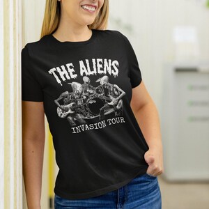 Puede incluir: Camiseta negra con un gr&aacute;fico blanco de tres extraterrestres tocando instrumentos. El texto "The Aliens Invasion Tour" est&aacute; impreso debajo del gr&aacute;fico.