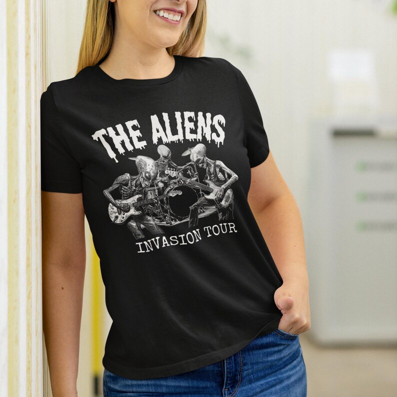 Puede incluir: Camiseta negra con un gr&aacute;fico blanco de tres extraterrestres tocando instrumentos. El texto "The Aliens Invasion Tour" est&aacute; impreso debajo del gr&aacute;fico.