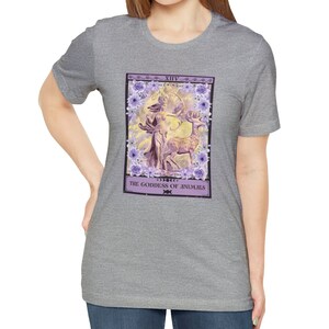 May include: A heather grey t-shirt with a purple and white tarot card design. The card depicts a woman with a bow and arrow, standing next to a deer. The card is titled "XIV The Goddess of Animals".