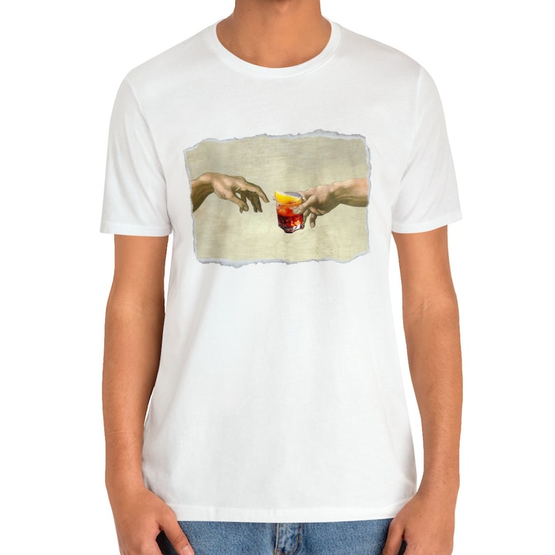 May include: A white t-shirt with a graphic of two hands reaching towards each other, holding a glass of red liquid with a lemon wedge. The graphic is a parody of the famous "Creation of Adam" painting.