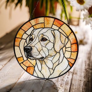 May include: Round stained glass window featuring a Labrador Retriever dog. The dog's head is depicted in shades of cream, beige, and brown, with a black outline. The background has orange and yellow hues. A black chain is attached for hanging.