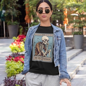 Peut inclure: Un t-shirt noir avec un design de carte de tarot vintage repr&eacute;sentant un squelette assis et r&eacute;fl&eacute;chissant. La carte est intitul&eacute;e "XVII The Overthinker".
