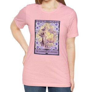May include: Pink t-shirt with a graphic of a tarot card depicting a woman with a bow and arrow standing next to a deer. The card is titled "The Goddess of Animals" and has the number XIV on it.