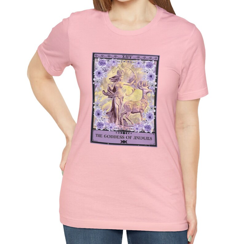 May include: Pink t-shirt with a graphic of a tarot card depicting a woman with a bow and arrow standing next to a deer. The card is titled "The Goddess of Animals" and has the number XIV on it.