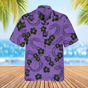 Pode incluir: Uma camisa de botões de manga curta roxa com um padrão de cobra preta e flores.